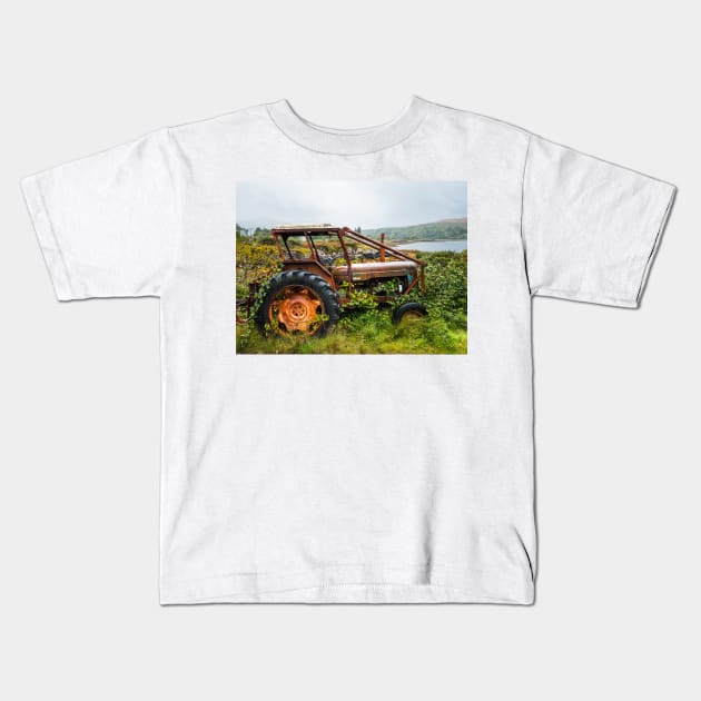 Old rusty tractor overgrown with weeds near a lake Kids T-Shirt by Dolfilms